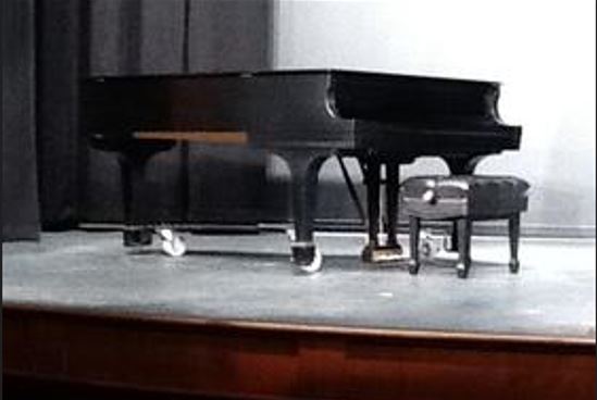 An image of a grand piano is shown on a stage with a spotlight on it.