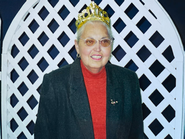 A photo of Janice Seagraves wearing a crown standing in front of a white trellis