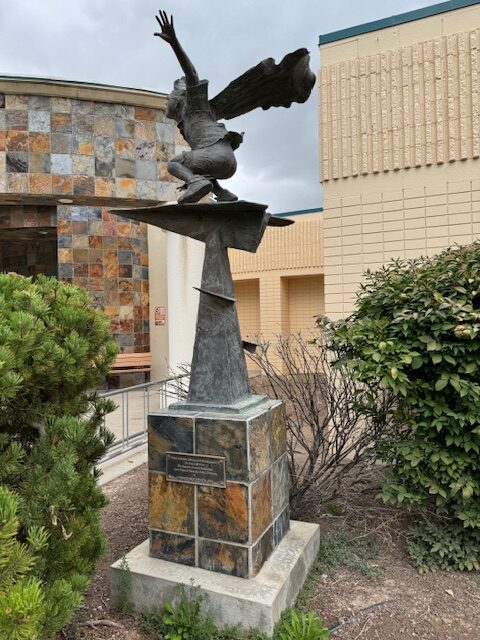 A large metal sculpture depicts a child flying on a paper airplane